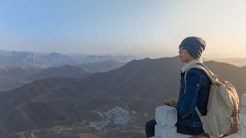 human woman sitting on wooden fence overlooking building background of mountain at daytime person