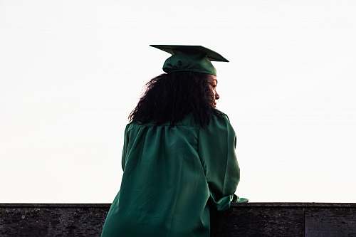 person woman standing at front of concrete fence wearing academic uniform human