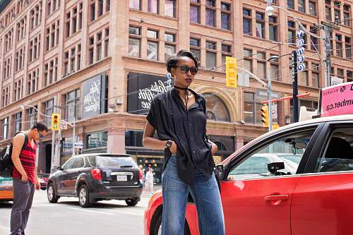 human woman standing near red car and concrete building during daytime car