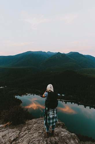 human woman standing on cliff taking picture of mountain person