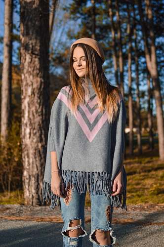 human woman standing while looking down and smirking near trees at daytime person