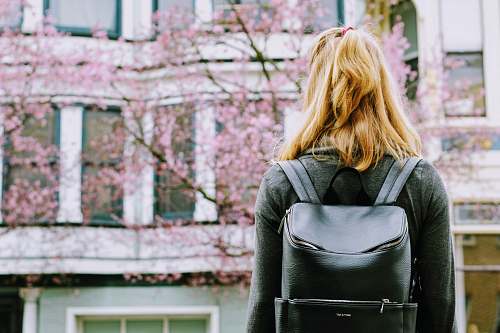 female woman wearing backpack facing concrete building woman