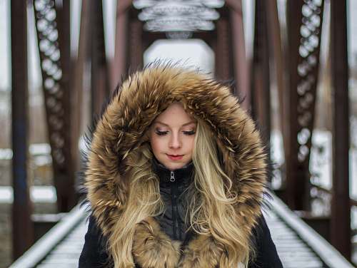 human woman wearing brown fur-lined hoodie standing on the bridge during daytime photography person