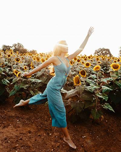 human woman wearing green sleeveless rompers standing and waving hands near garden of sunflower at daytime flower