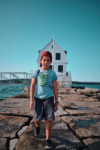 human boy standing near white house beside body of water people