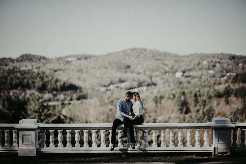 human couple sitting on ledge in distant of mountain people