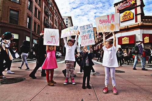 people four children raising up a banner at the middle of a busy street during day time signs