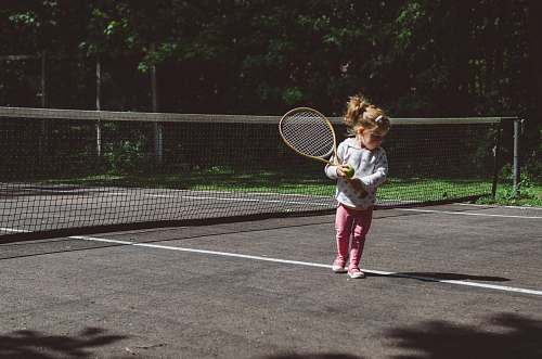 people girl holding lawn tennis racket while standing beside white and black net human