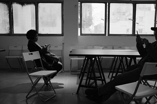 black-and-white grayscale photo of two person sitting on chair inside the room chair