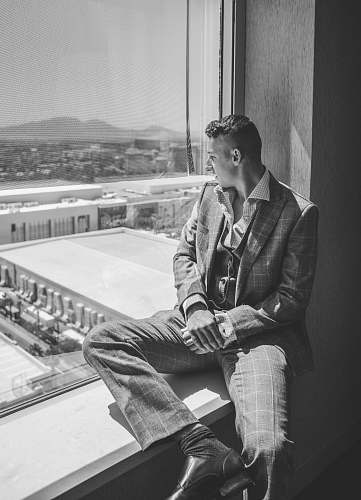 black-and-white grayscale photography of man sitting on window grey