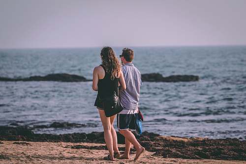 human man and woman walking by the beach during daytime people