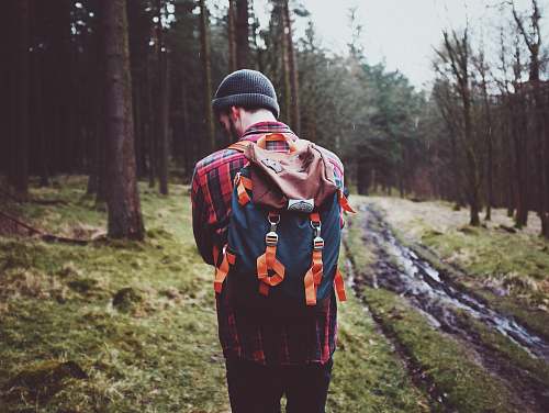 human man carrying backpack standing surrounded by tree people