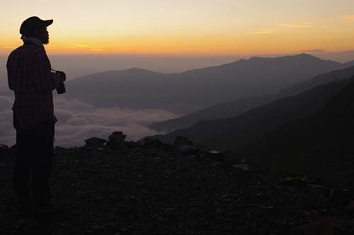 human man carrying camera facing sideways looking at the mountain range people