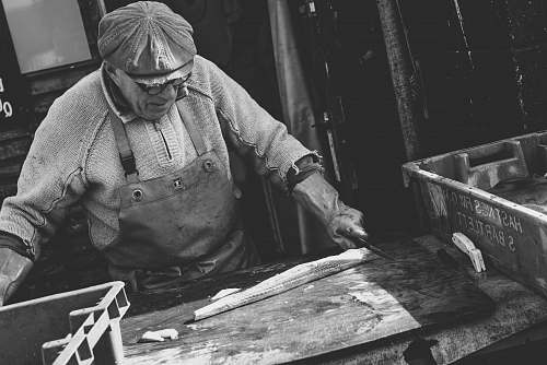 human man holding knife chopping white substance on brown wooden board black-and-white