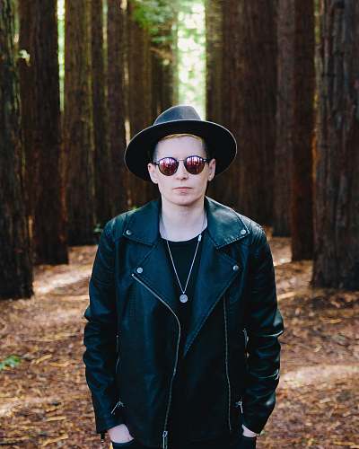 human man in black full-zip jacket standing between green trees man