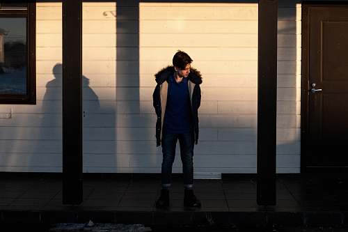 human man in black fur jacket standing in the middle of wooden posts people