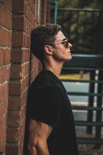 human man in black short-sleeved shirt leaning on brow brick wall leaning