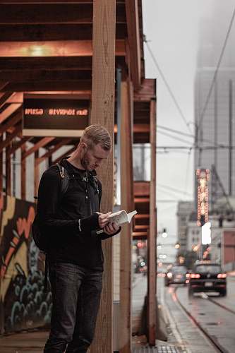 people man in black sweater stands on sidewalk with book in hand human