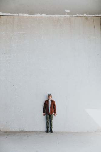 human man in brown coat standing by the white wall people