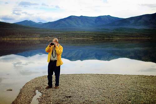 human man in yellow jacket taking pictures during daytime people