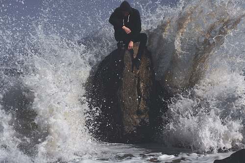 sea man seating on stone in between waving sea ocean