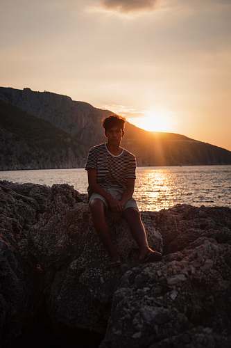 people man sitting on rock near sea at golden hour human