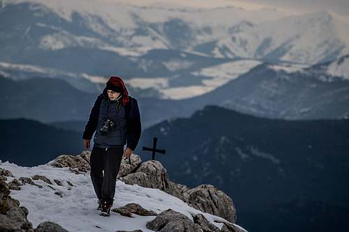 human man standing on peak near cross at daytime people