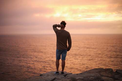 human man standing on rock near seashore during sunset people