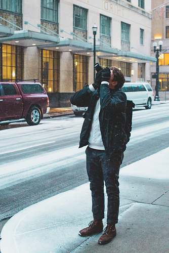 vehicle man standing on sidewalk holding DSLR camera taking picture above car