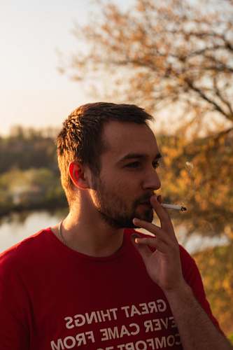 people man standing smoking cigarette near body of water and trees human