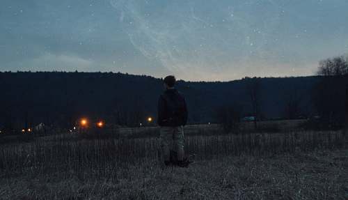stars man wearing black jacket standing near grass looking at mountain field