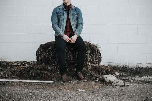 human man wearing blue denim western shirt sitting next to white concrete wall people