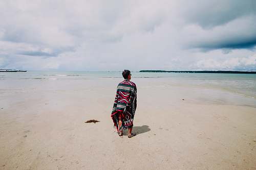 beach man wearing red and green scarf facing body of water ocean