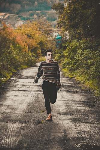 human man wearing sweater running on road between trees during daytime people