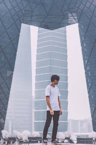 human man wearing white crew-neck shirt standing near the building people