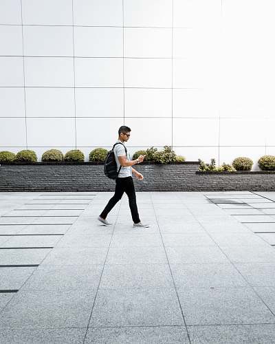 human man with backpack using phone walking alone on pathway people