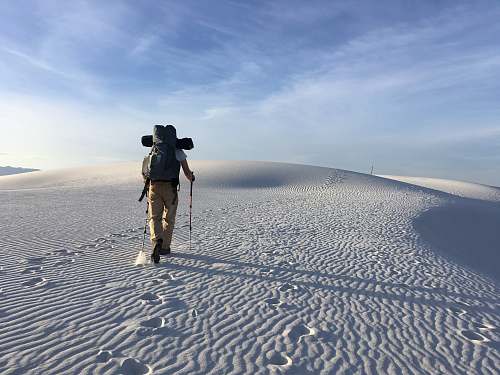 human person hiking on sand dunes under white skies during daytime people