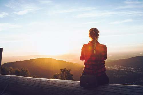 people person sitting on wood fence facing mountain under cloudy sky human