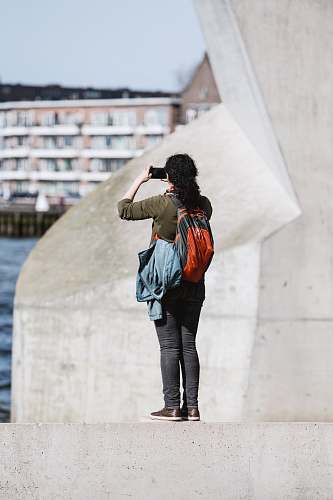 human person standing on concrete edge holding up smartphone taking photo people