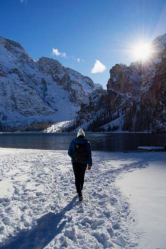 mountain person walking on snow near body of water and mountains snow