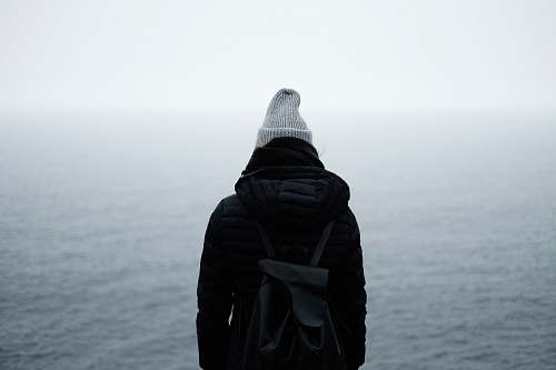 people person wearing black jacket standing in front of the ocean backpack