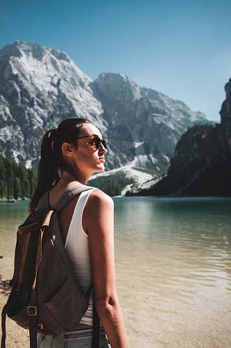 human photo of woman wearing white tank top and gray backpack standing near body of water people