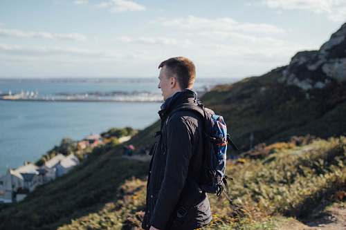 human shallow focus photography of man standing on mountain looking at large body of water people