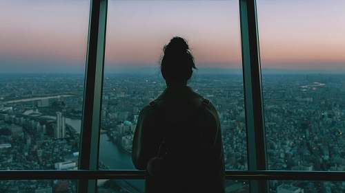 people silhouette of person standing inside the building facing the glass mirror watching the city human