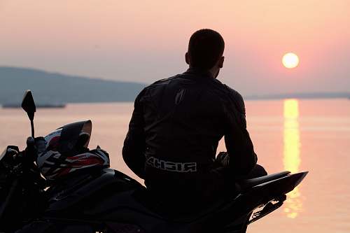 human silhouette photo of man sitting on sports bike beside sea during golden hour motorcycle