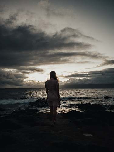 human silhouette photography of woman standing near sea waves people
