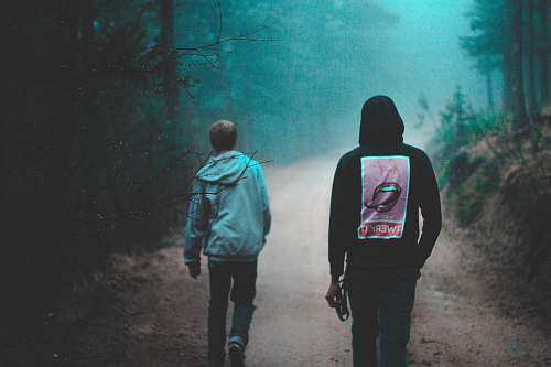 human two person walking on dirt road between green trees people