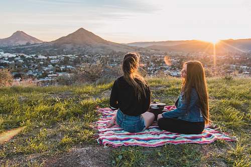 people two women having picnic facing mountain and buildings during golden hour human