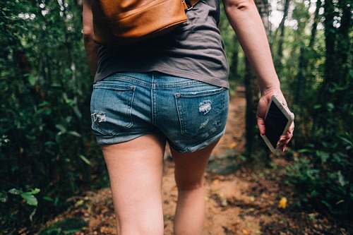 human woman holding phone walking toward trees people