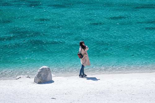 human woman in brown coat beside body of water during daytime people
